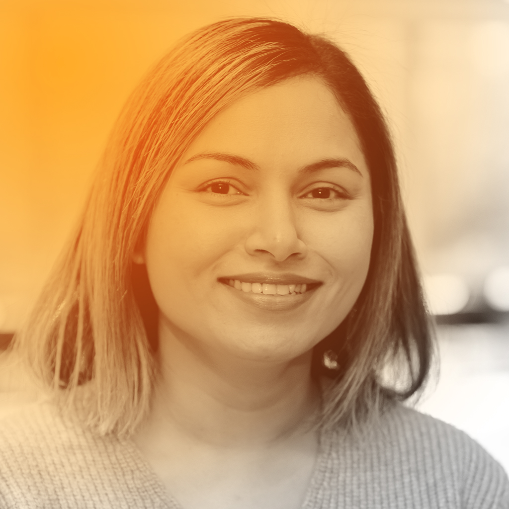 Camy's portrait. She's an Indian woman with short light brown hair and a wide smile. She's wearing a dark coloured t-shirt.