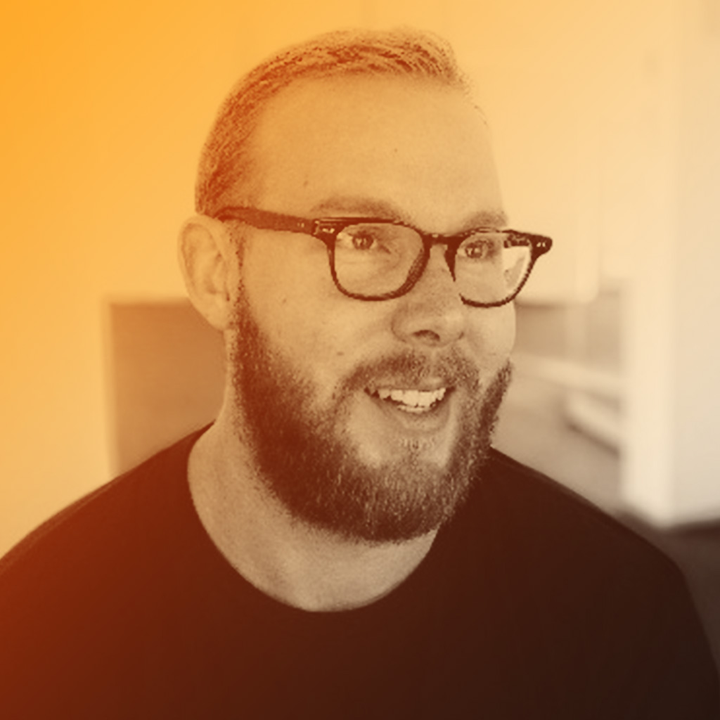 Marcus's portrait. Marcus is wearing a black t-shirt and glasses.