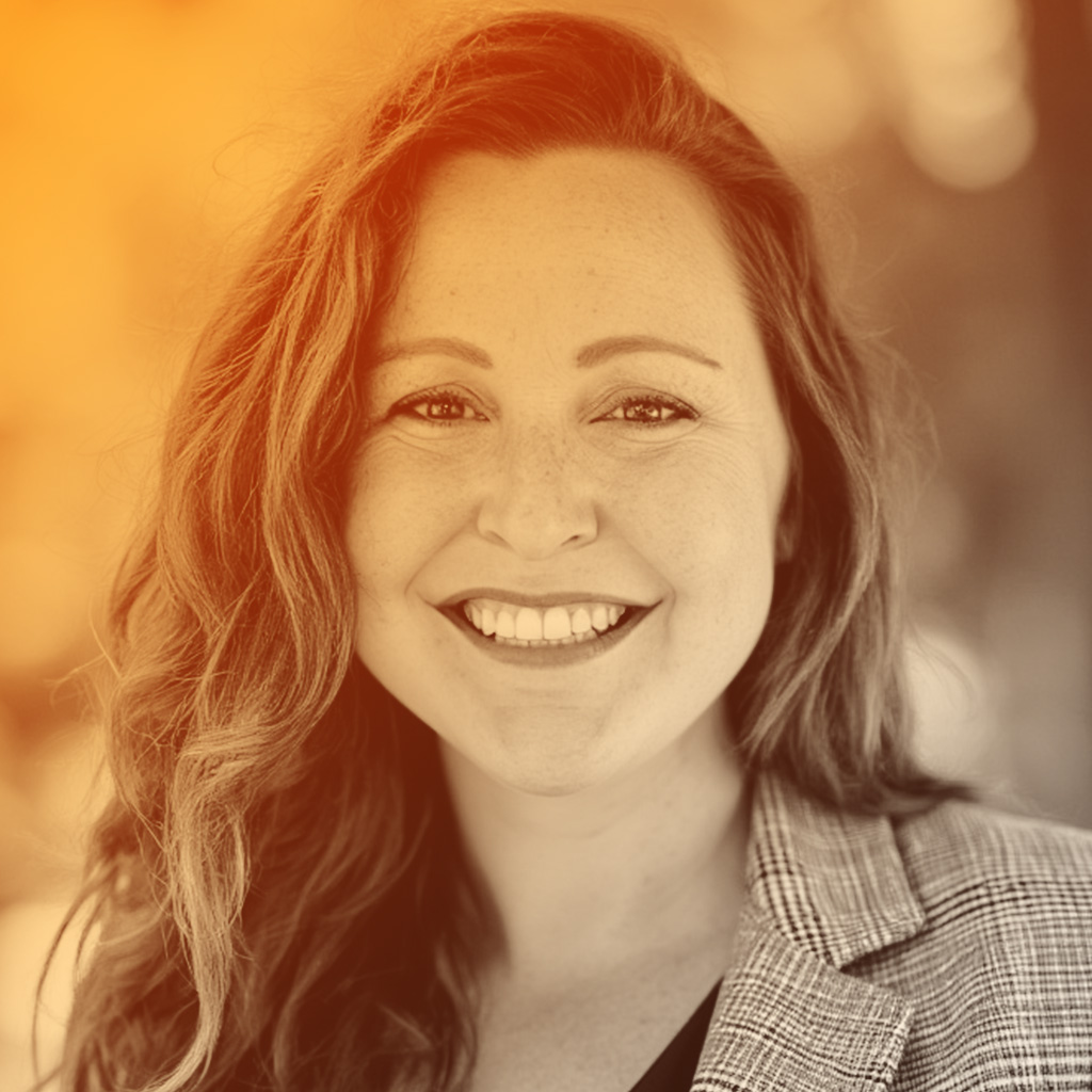 Michelle's portrait. Michelle is wearing a black top underneath a check blazer, and she is smiling at the camera.