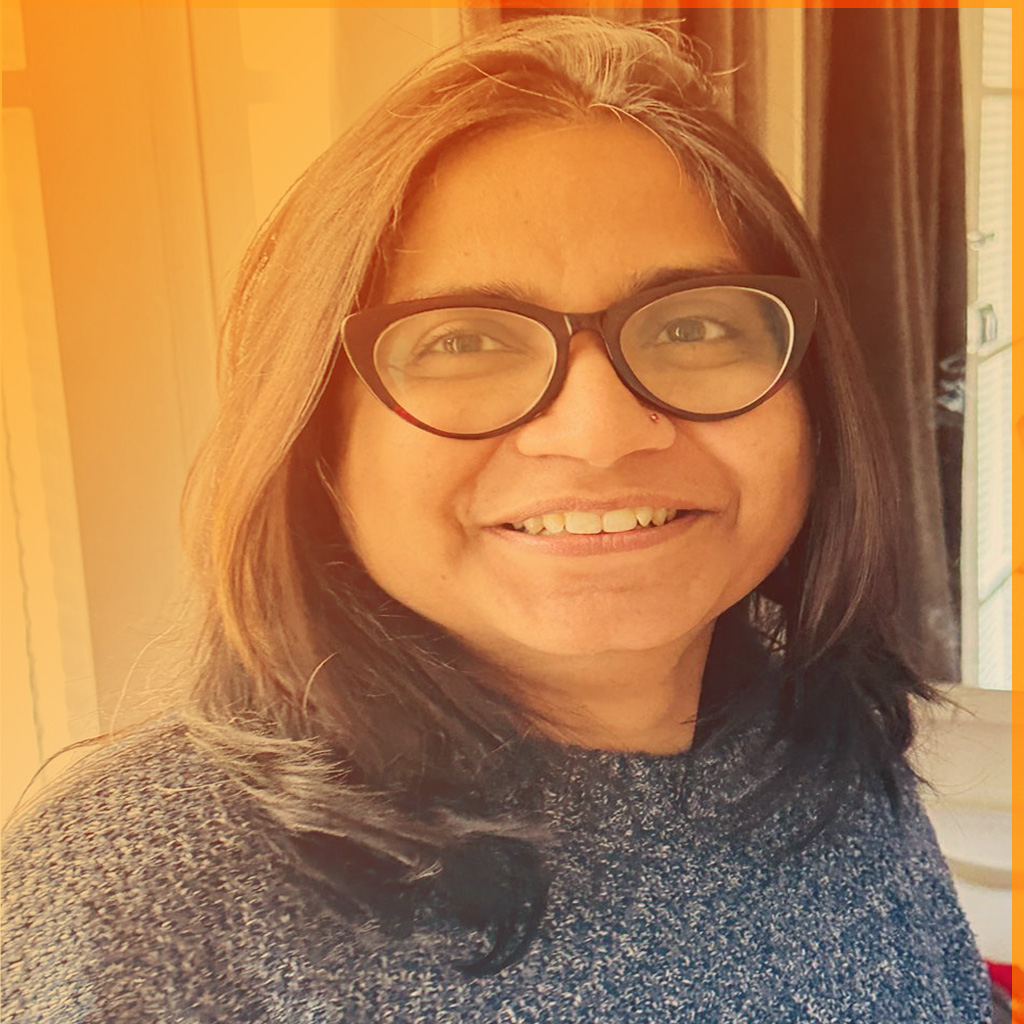 Tarannum's portrait. She's an Indian woman with dark brown hair and a wearing glasses. She's wearing a blue coloured jumper.