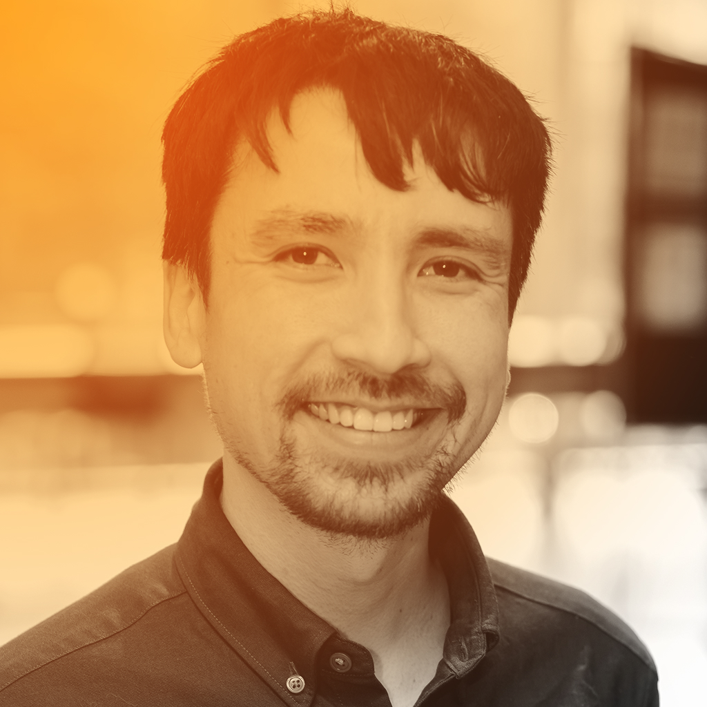 Tim's portrait. A smiling half Singaporean man with short dark and some facial hair. He's wearing a plaid shirt.